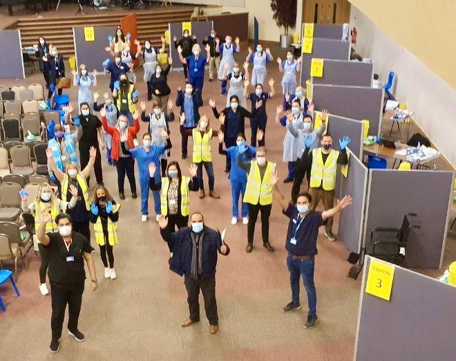 Image shows a large group of people waving to the camera. Some are wearing high visibility jackets.