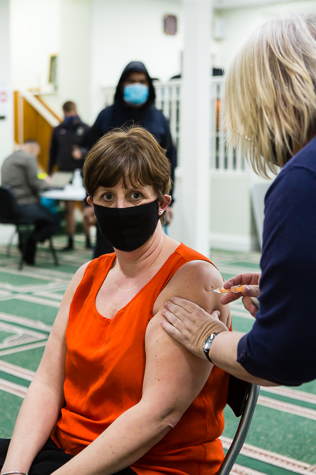 Woman sat down receives vaccine in left arm